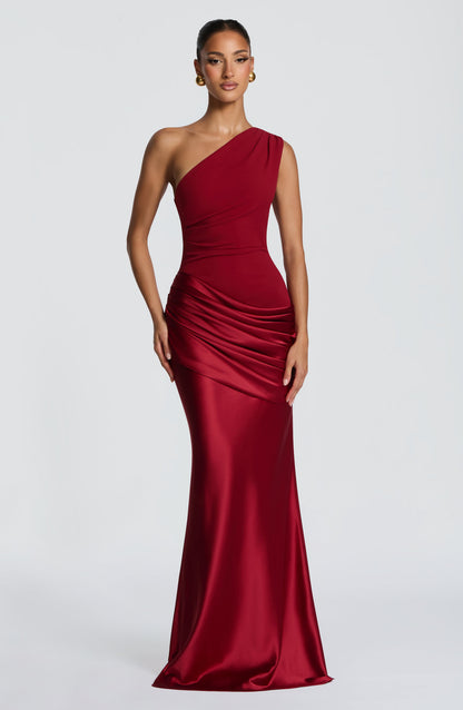 Front view of the deep red one-shoulder maxi dress with ruched satin hip drape and gold ball earrings. 15