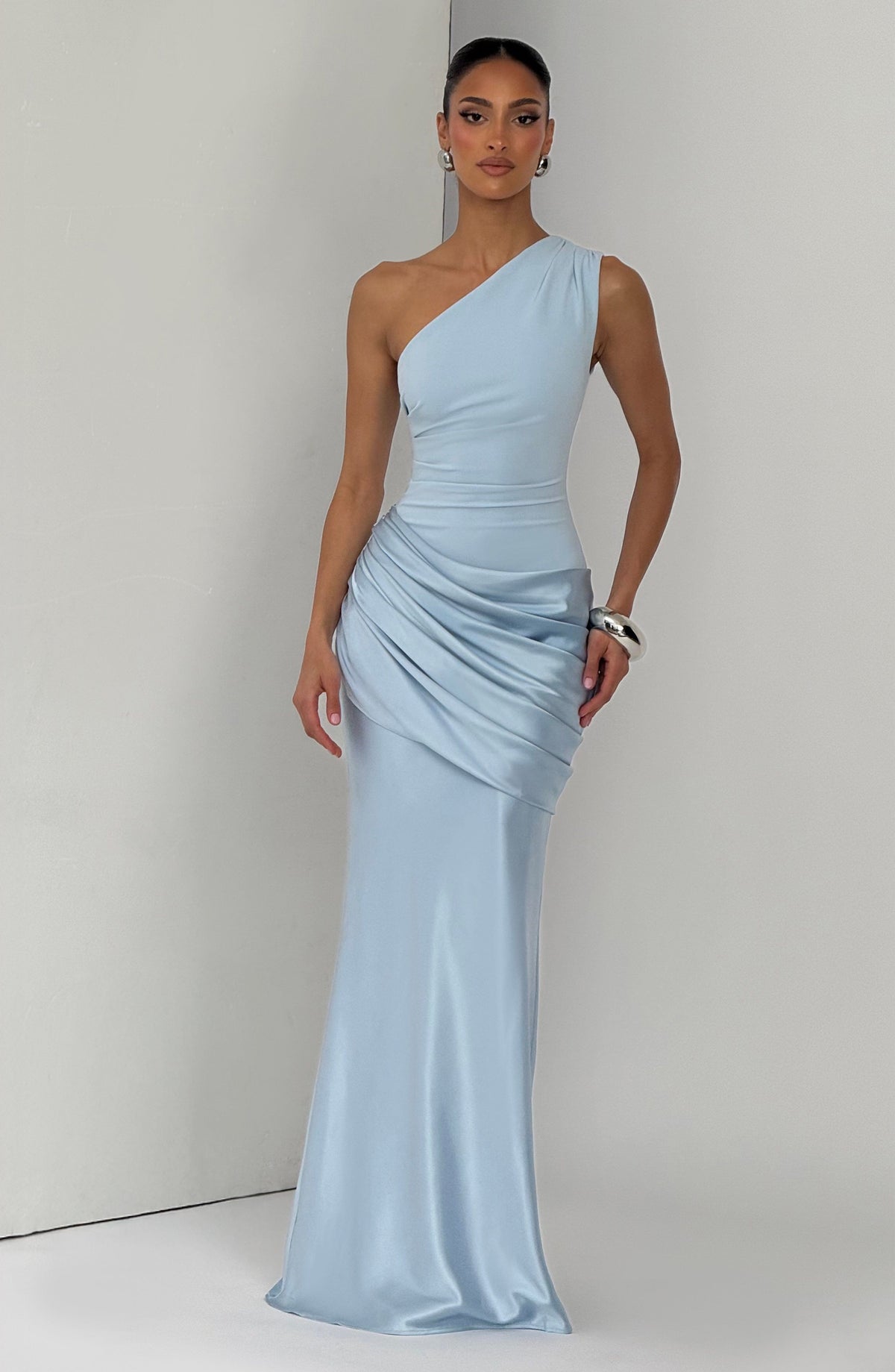 Pale blue one-shoulder satin maxi dress worn by a model standing against a light grey backdrop. 4