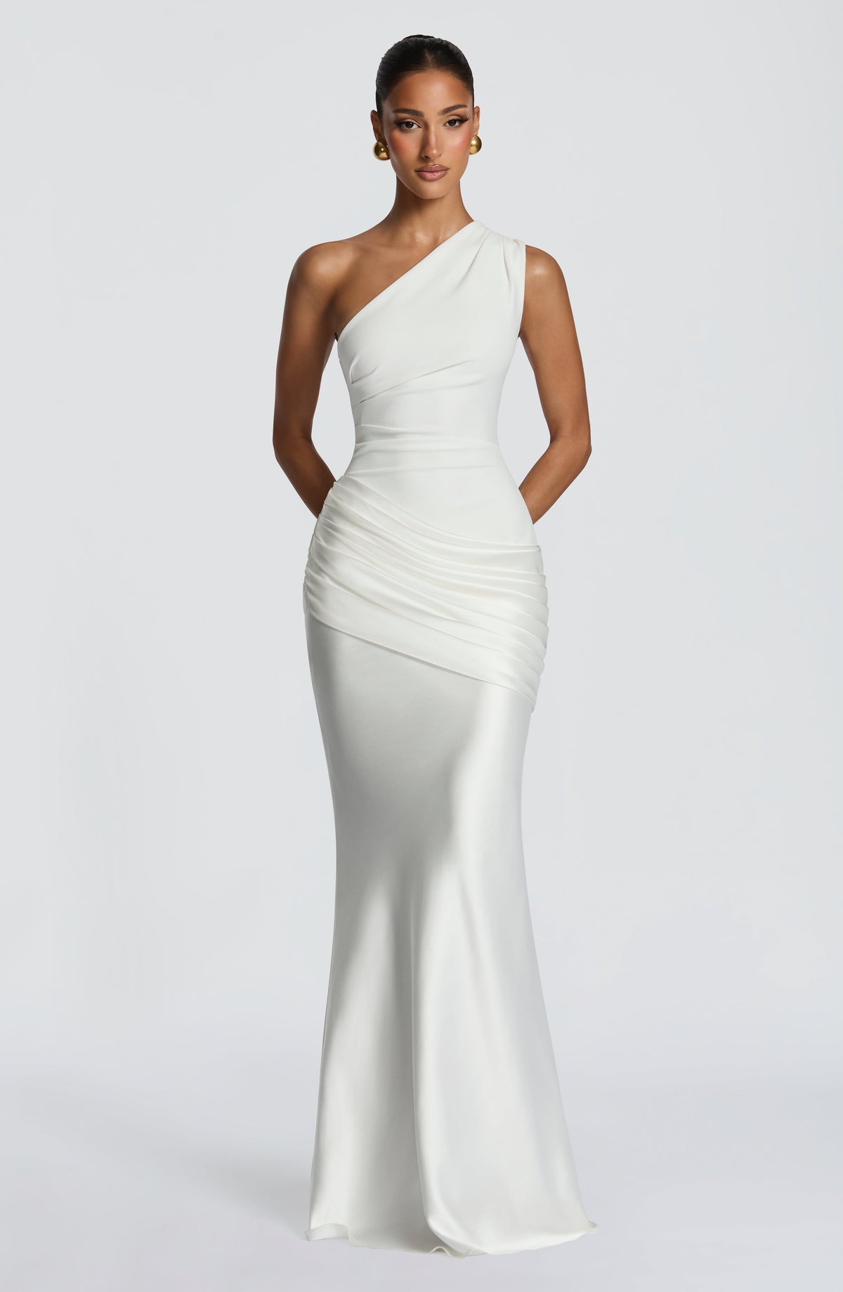 Straight-on front view of the white one-shoulder dress with the model's hands clasped behind her, full length to the floor. 25