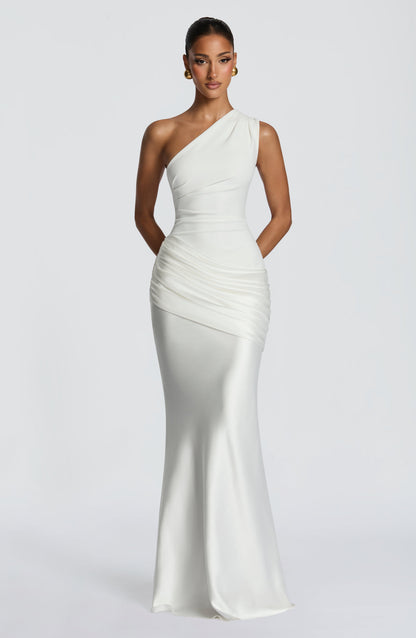 Straight-on front view of the white one-shoulder dress with the model's hands clasped behind her, full length to the floor. 25