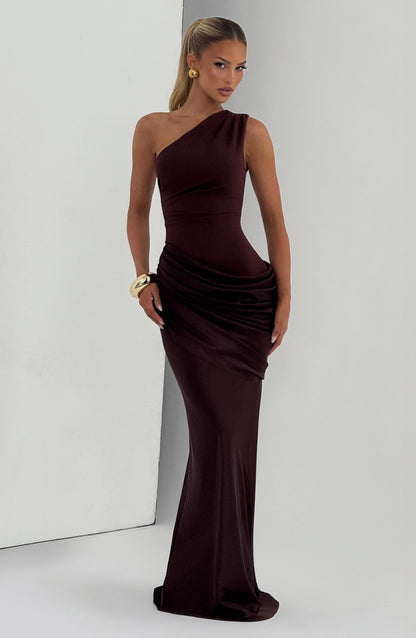 Brown one-shoulder maxi dress with draped hip panel, styled with gold earrings and a chunky gold cuff. 9