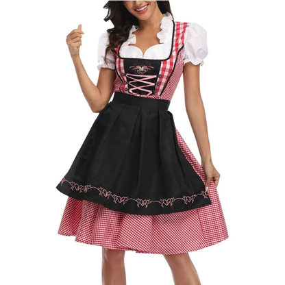Close front view of the dirndl in red gingham with a black apron and pink heart embroidery, worn by a smiling model. 1