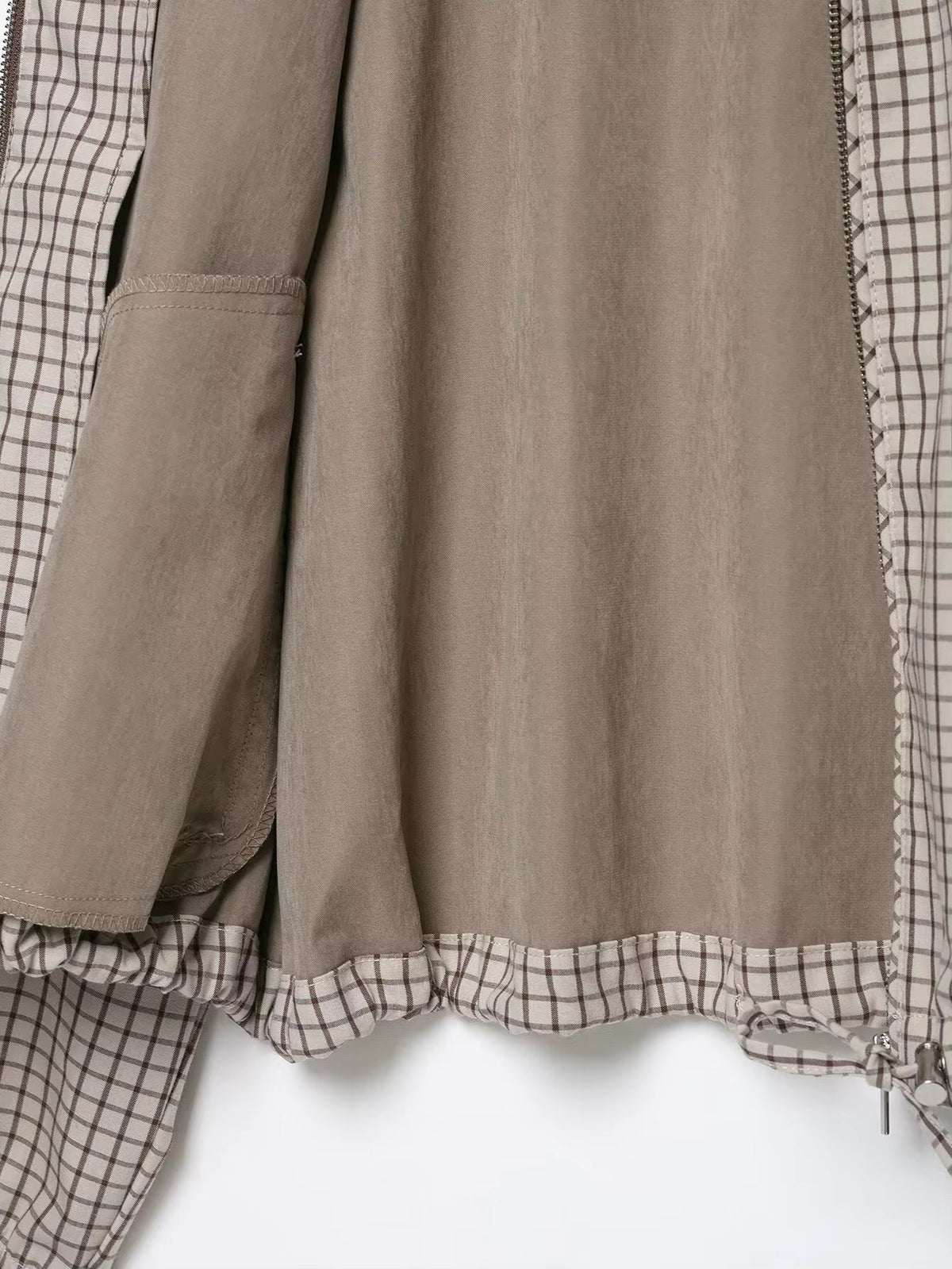 Flat lay of the jacket's open lower half, showing the plain taupe lining, inner pocket and checked drawstring hem. 5