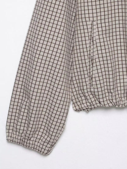 Detail of the checked sleeve with elasticated cuff and a side pocket above the gathered hem, laid flat. 8