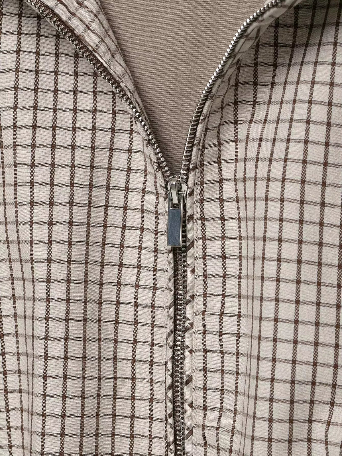 Close-up of the silver zip pull and teeth running down the checked front, with the lining visible at the opening. 6