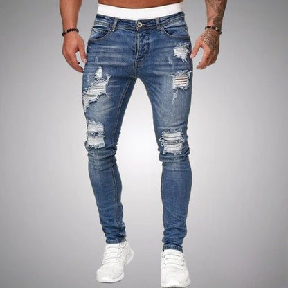 Front view of slim-fit ripped jeans in medium blue, worn by a model with white trainers, showing frayed distressing on the thighs and knees. 3