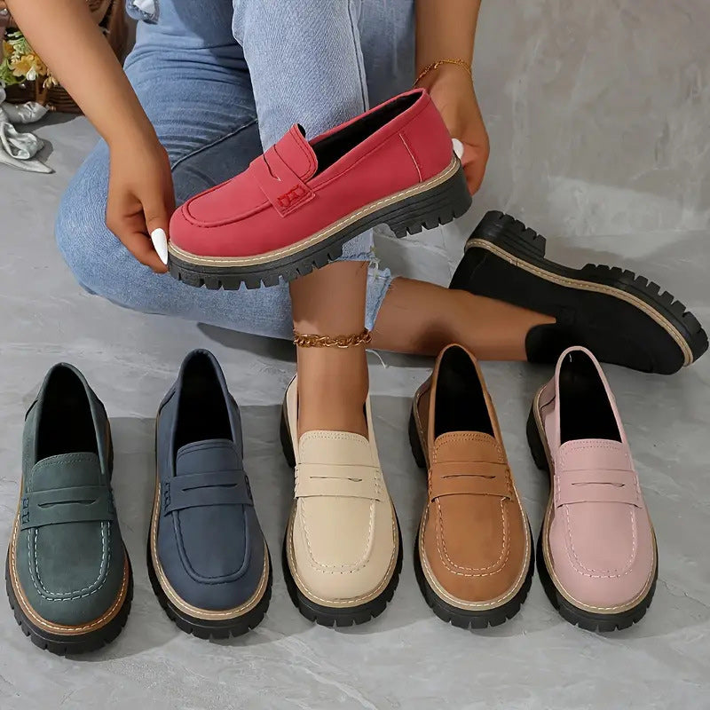 Colour range of the loafers: red held in hand, with green, navy, cream, tan, pink and black pairs arranged on the floor. 2