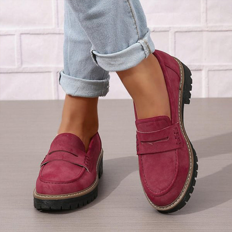 Burgundy suede-look penny loafers with thick treaded soles, worn with rolled light blue jeans on a grey floor. 4