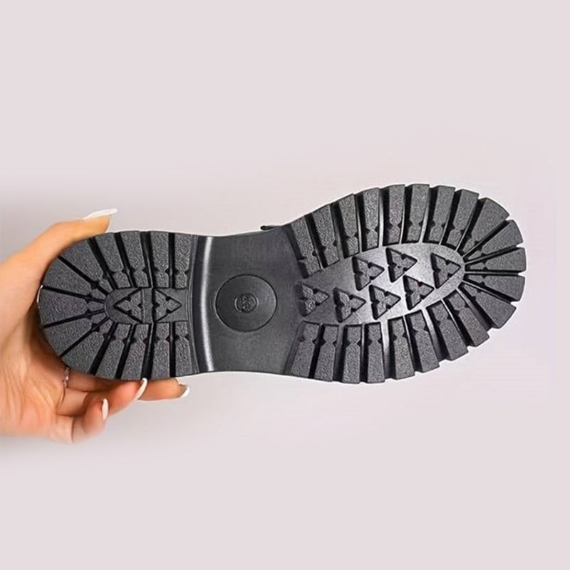 Underside of a loafer held in a hand, showing the deep black tread pattern of the chunky rubber sole. 10