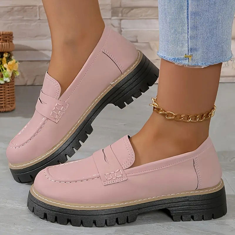 Pink smooth-finish loafers with stitched penny strap and thick black platform sole, worn with a gold ankle chain. 11