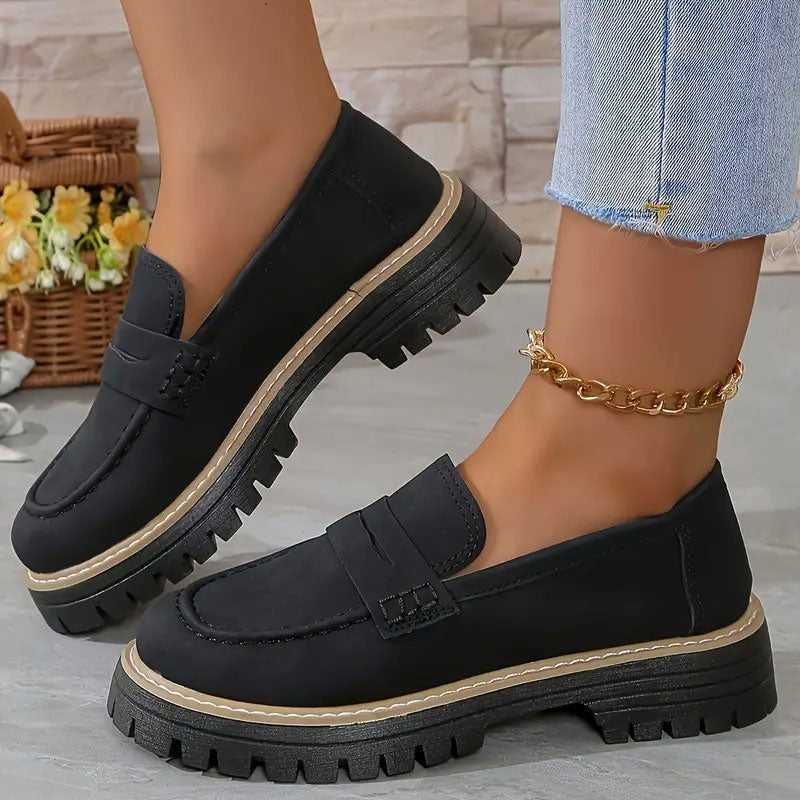 Black suede-look loafers with tan welt stitching and a chunky platform sole, worn with a gold ankle chain. 12
