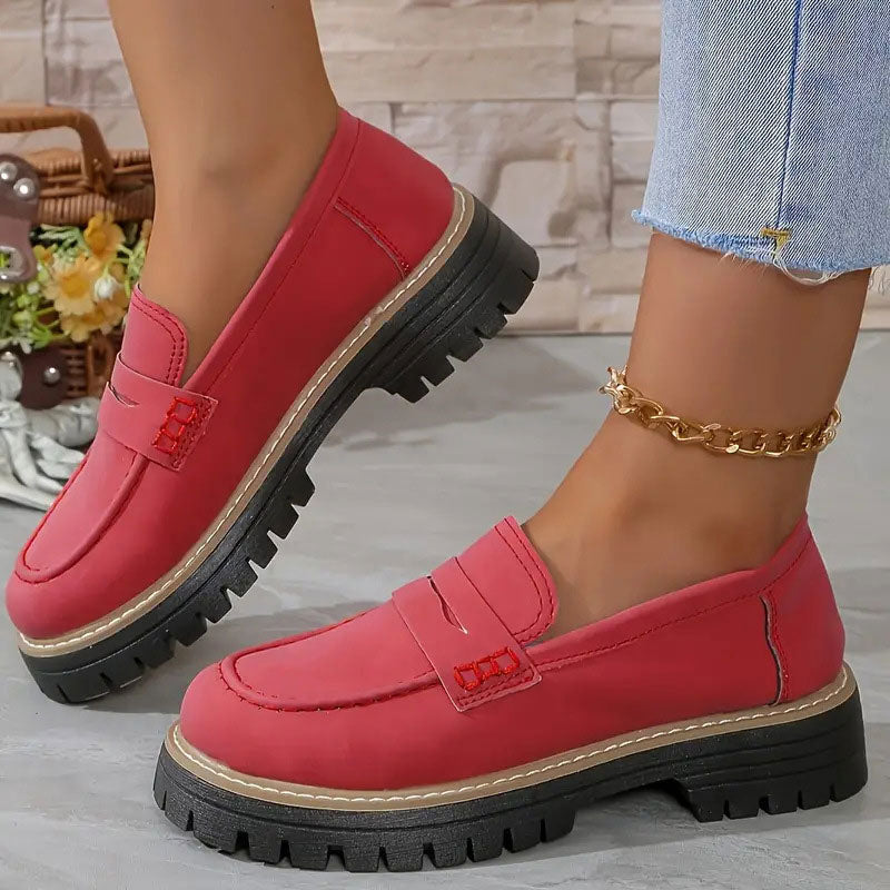 Red loafers with matching red stitching on the penny strap and a chunky black platform sole, worn with a gold anklet. 13