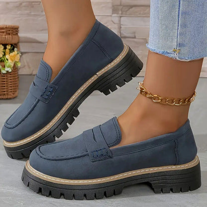 Navy blue suede-look loafers with a tan welt and chunky black platform sole, worn with a gold chain anklet. 16