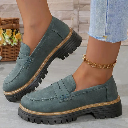 Teal-green suede-look loafers with a tan welt and thick black treaded platform sole, worn with a gold ankle chain. 15