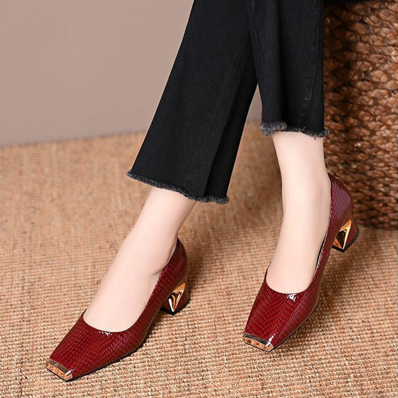 Burgundy red snake-effect pumps with gold toe caps and angular gold-detail heels, worn with frayed black trousers on a woven mat. 2
