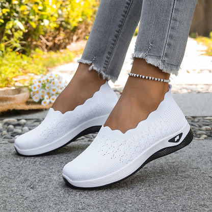 White knit slip-on shoes with a scalloped collar and white sole, worn outdoors with frayed grey jeans and a beaded anklet. 1
