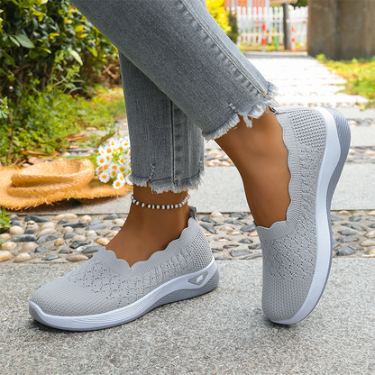 Light grey knit slip-on shoes with a scalloped collar and white midsole, worn with frayed jeans beside a straw hat. 3