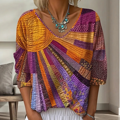 Close-up of the sunburst patchwork blouse in orange, purple and magenta tones, worn with white trousers and a turquoise statement necklace. 2