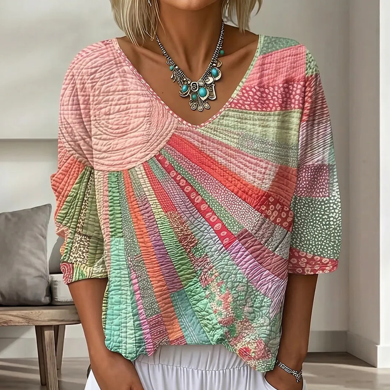 Close-up of the sunburst patchwork blouse in soft pink, coral and mint green, with three-quarter sleeves, worn with a turquoise necklace. 3