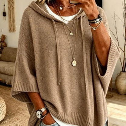 Torso view of the khaki hooded jumper with drawstrings and ribbed cuffs, worn over a white top with gold necklaces. 14