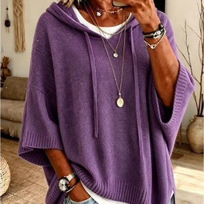 Torso view of the purple hooded jumper with drawstrings and wide ribbed sleeves, layered over a white top with necklaces. 11