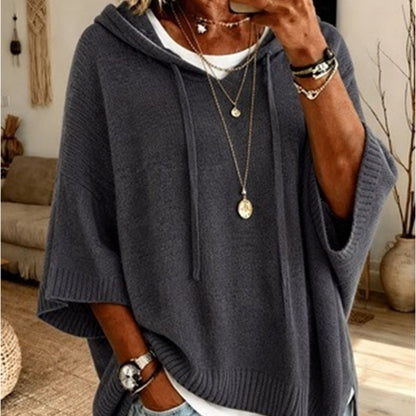 Torso view of the dark grey hooded jumper with drawstrings and ribbed cuffs, layered over a white top with gold necklaces. 9