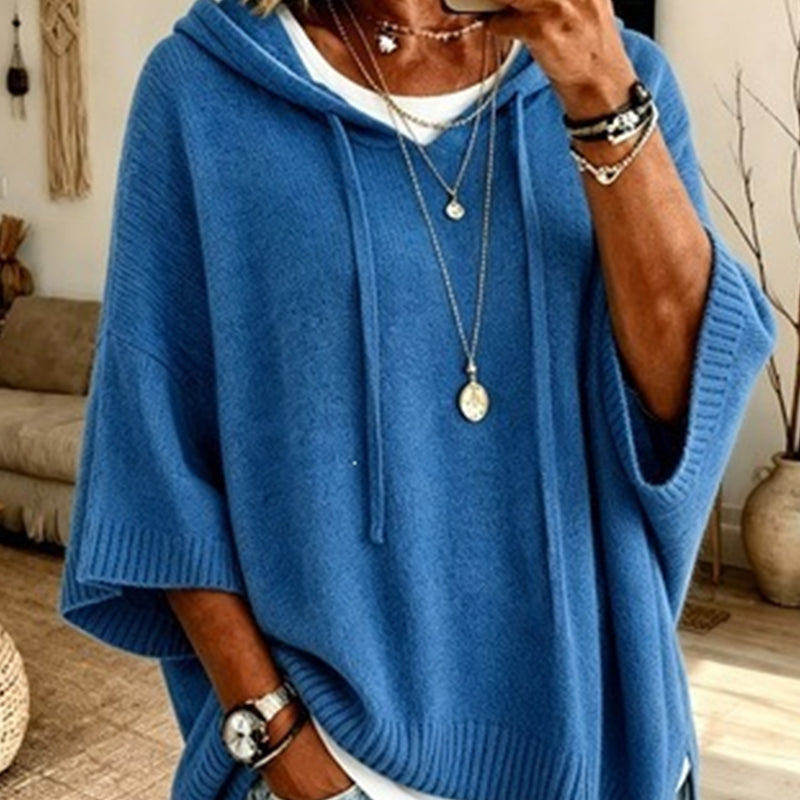 Torso view of the bright blue hooded jumper with drawstrings and ribbed trims, worn over a white top with necklaces. 12