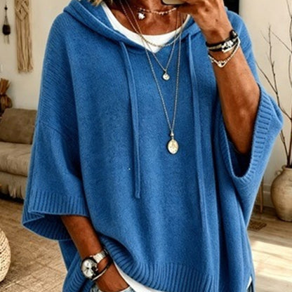Torso view of the bright blue hooded jumper with drawstrings and ribbed trims, worn over a white top with necklaces. 12
