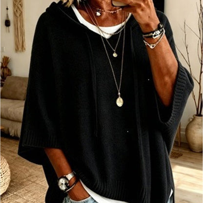 Torso view of the black hooded jumper with drawstrings and ribbed hem, worn over a white top with gold necklaces. 10