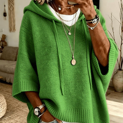 Torso view of the green hooded jumper with drawstrings and ribbed cuffs, layered over a white top with gold necklaces. 19