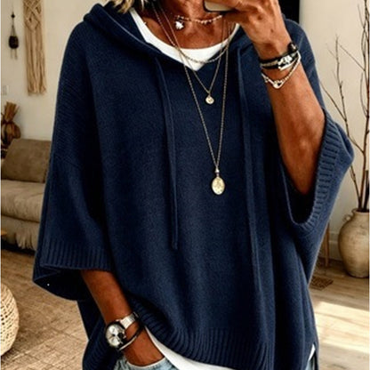 Torso view of the navy blue hooded jumper with drawstrings and ribbed hem, layered over a white top with necklaces. 15