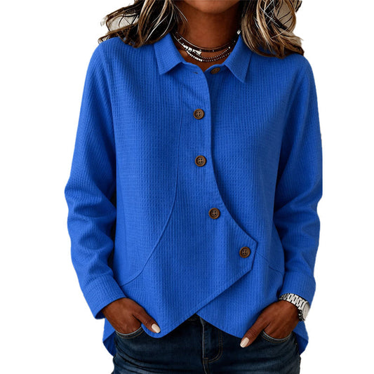 Model wearing the waffle-knit jumper in bright blue, hands in jeans pockets, showing the collar, brown buttons and curved asymmetrical hem. 1