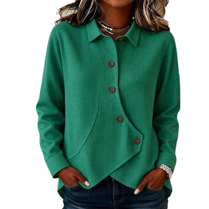 Model wearing the waffle-knit jumper in green, hands in jeans pockets, showing the collar, brown buttons and curved asymmetrical hem. 2