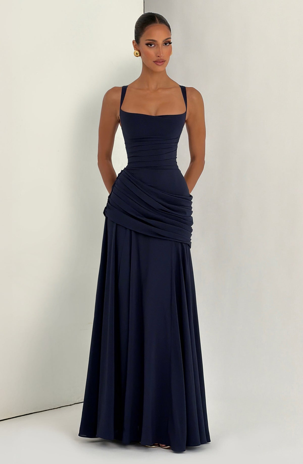 Navy dress modelled against a plain cream wall, hands tucked in pockets, showing the full length 11