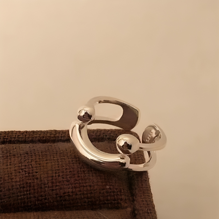 Silver ring angled on a woven brown surface, showing the glossy balls, curved bar and open back of the band. 5
