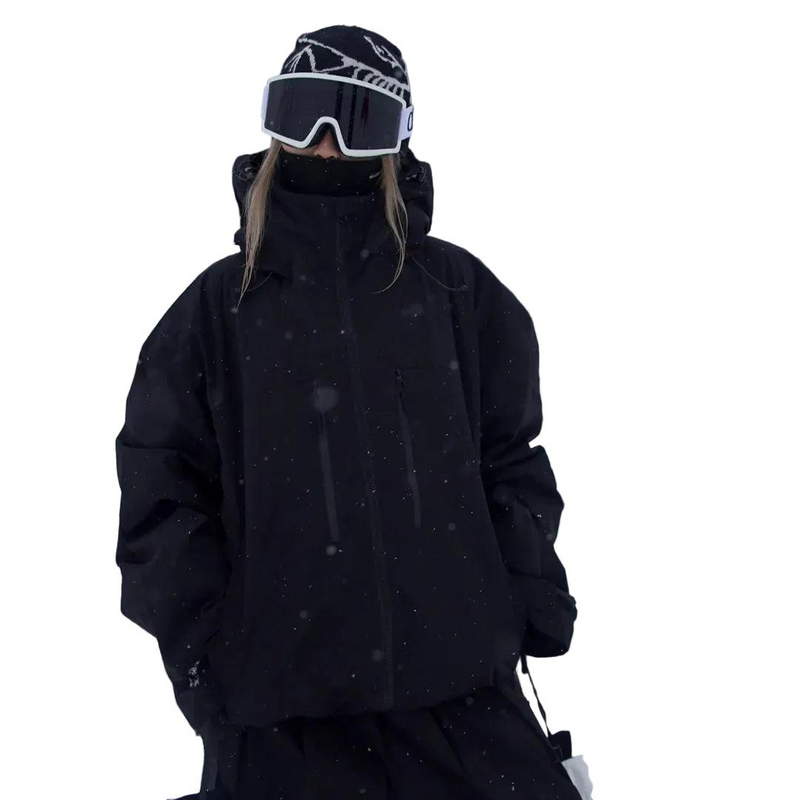 Model wearing the jacket in black with a high collar, goggles and a beanie, in falling snow 3