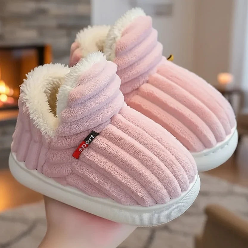 Pink ribbed plush slippers with fleece-lined openings held in a hand beside a glowing fireplace. 4