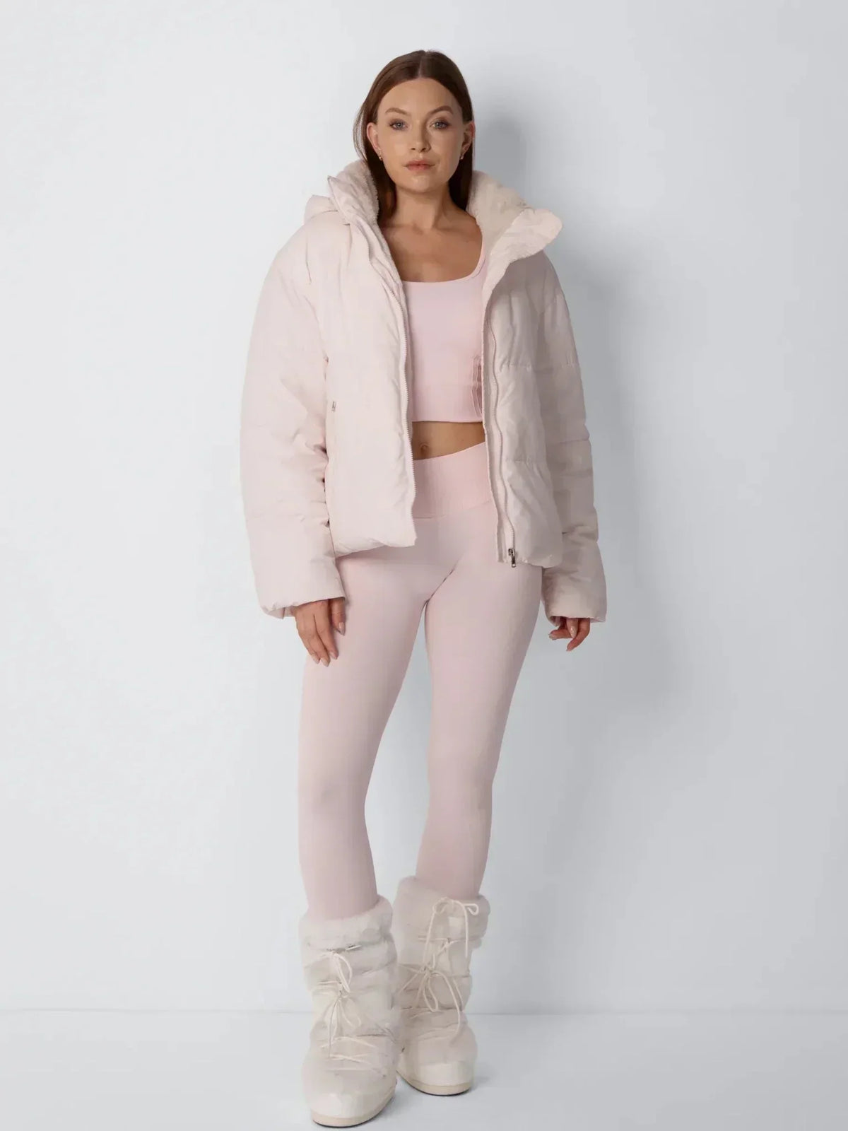 Full-length front view of a pale pink puffer jacket worn open over a matching crop top and leggings 10