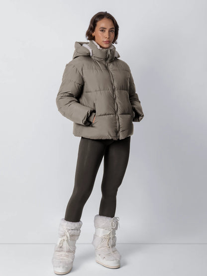 Full-length view of a model in a taupe puffer jacket with fleece collar, dark leggings and white fur boots 21