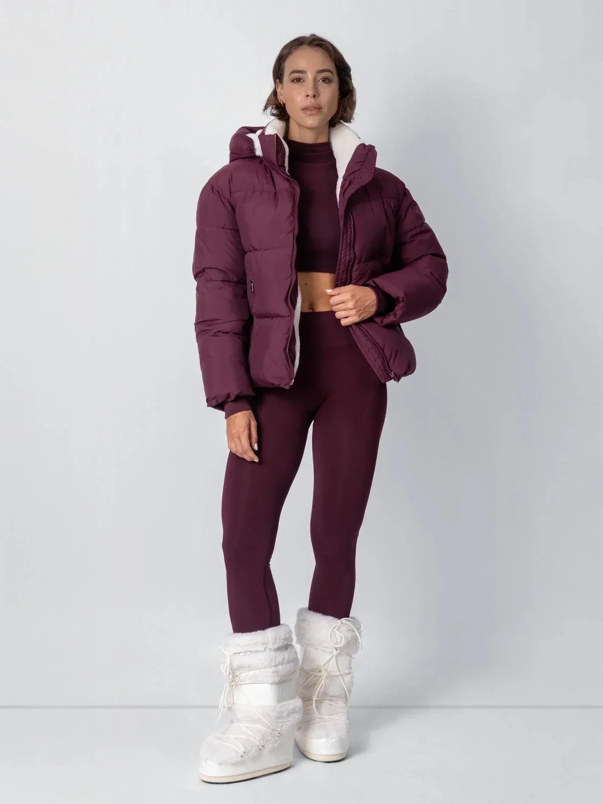 Full-length view of a burgundy puffer jacket worn open with matching leggings and fluffy white boots 17