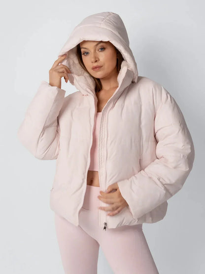 Model in a pale pink puffer jacket with the hood up, touching the hood edge and showing the fleece lining 6
