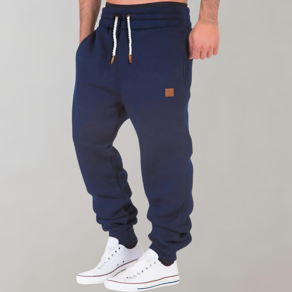 Model wearing navy blue joggers with white drawstring and tan patch, hand in pocket, with white trainers 5
