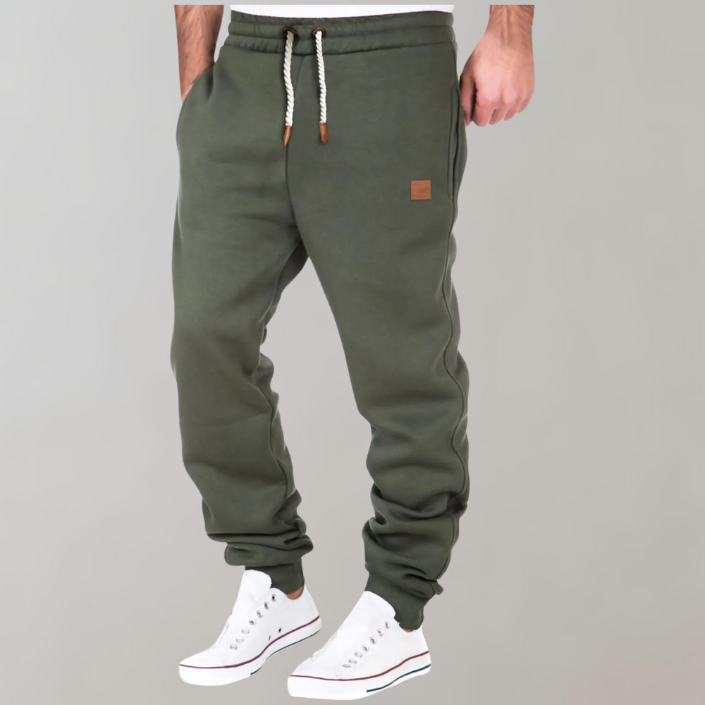 Model wearing olive green joggers with white drawstring and small tan patch, hand in pocket, white trainers 3