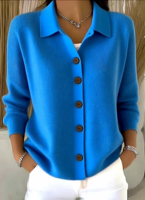 Model wearing the bright blue version of the collared knit cardigan, buttoned down the front, with hands in pockets. 4