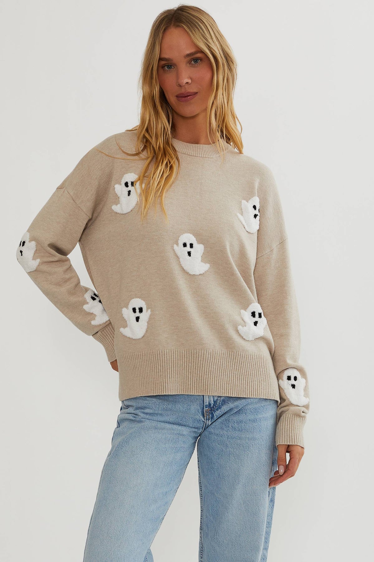 Model facing the camera in the beige jumper with fluffy white ghosts, worn with light blue jeans 1
