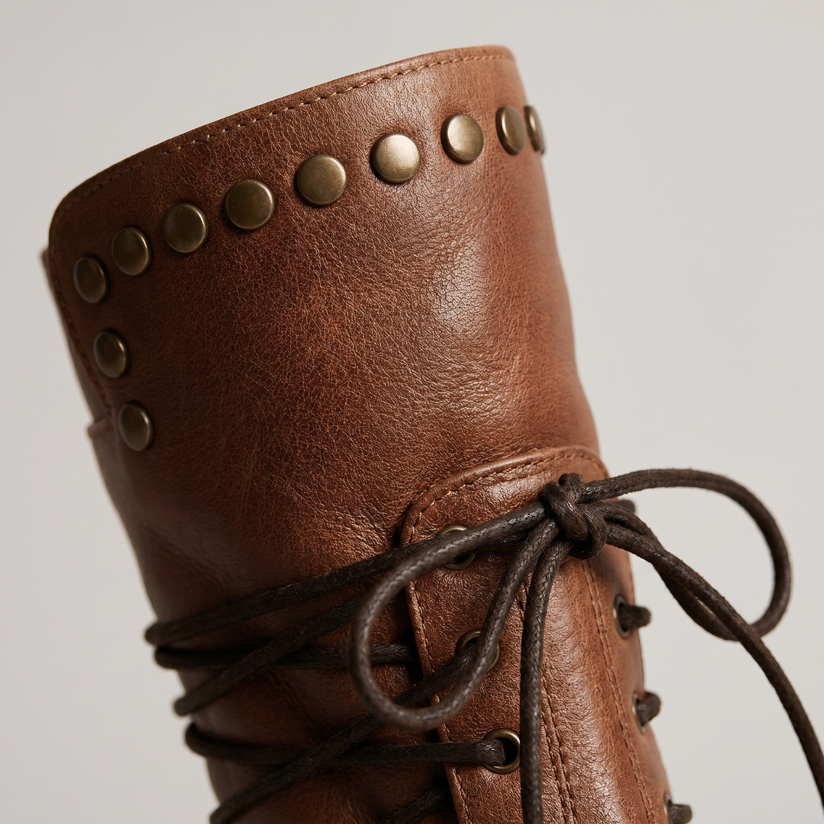 Close-up of the studded collar and knotted dark laces on a tan brown leather boot. 3