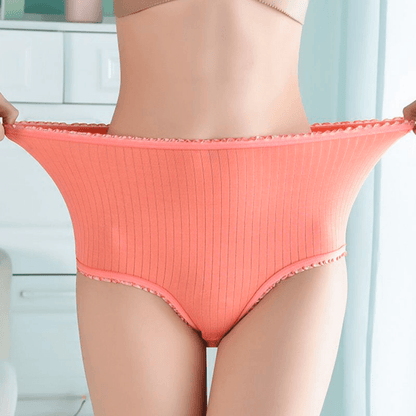 Model stretching the waistband of coral ribbed high-waisted briefs outwards to show how elastic the fabric is, with frilly trim. 1