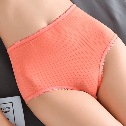 Close-up of coral ribbed high-waisted briefs worn by a model lying down, showing the frilled edging at waist and leg openings. 2