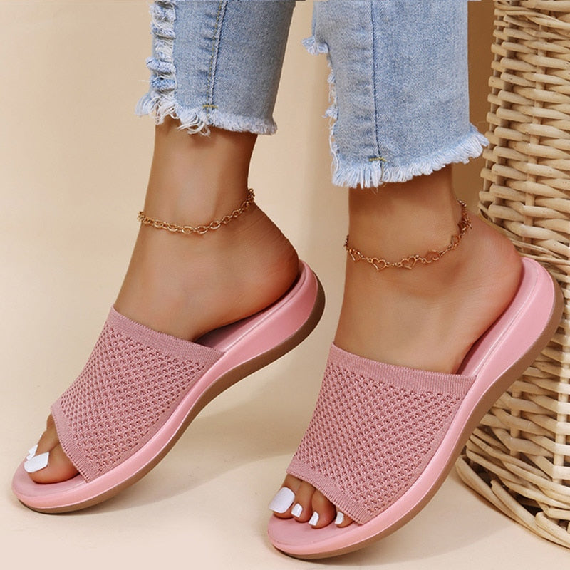 Worn slides in coral pink with a perforated knit strap, shown with frayed jeans and ankle chains 1