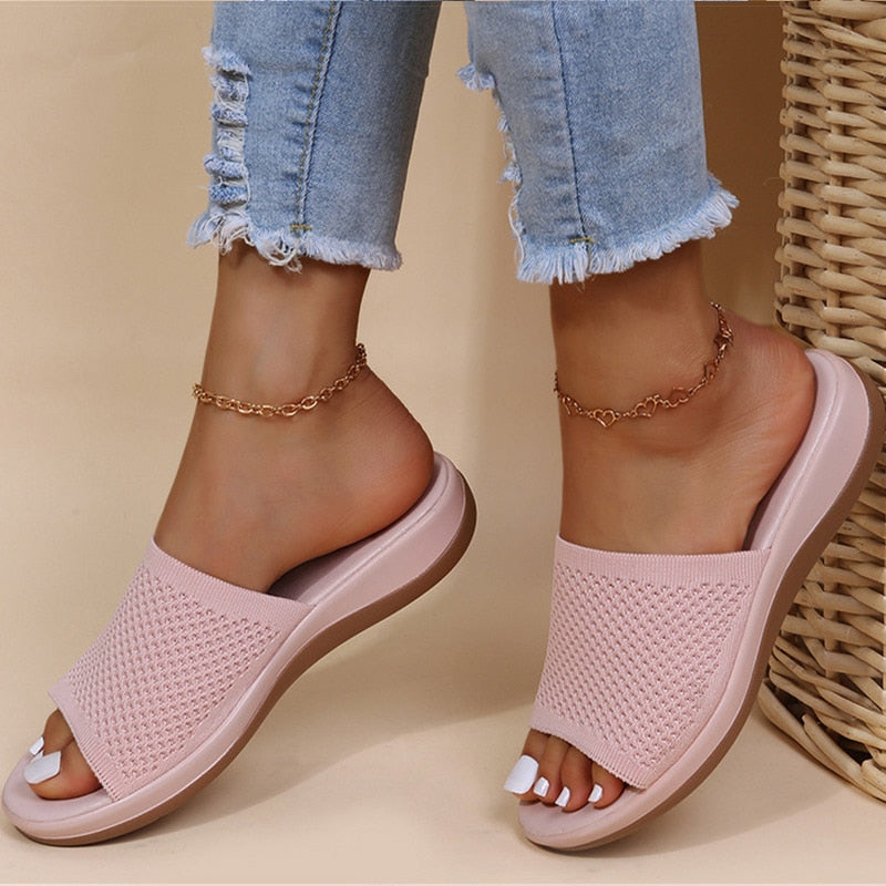 Slides in soft pale pink with a breathable knit strap, worn on feet beside wicker 4